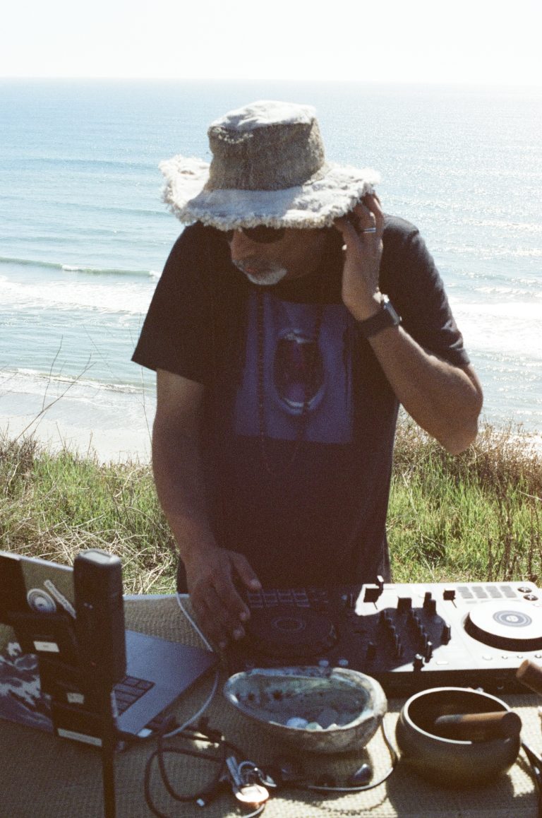 bhoosh mixing music at an outdoor DJ setup overlooking the ocean.