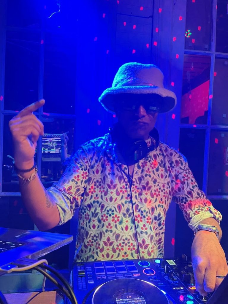 bhoosh mixing music in a bucket hat and sunglasses under blue and red club lighting.