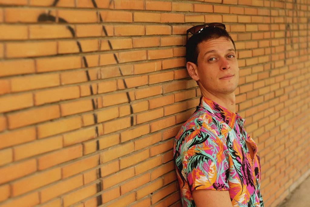 Caiio leaning against a brick wall in a colorful patterned shirt.