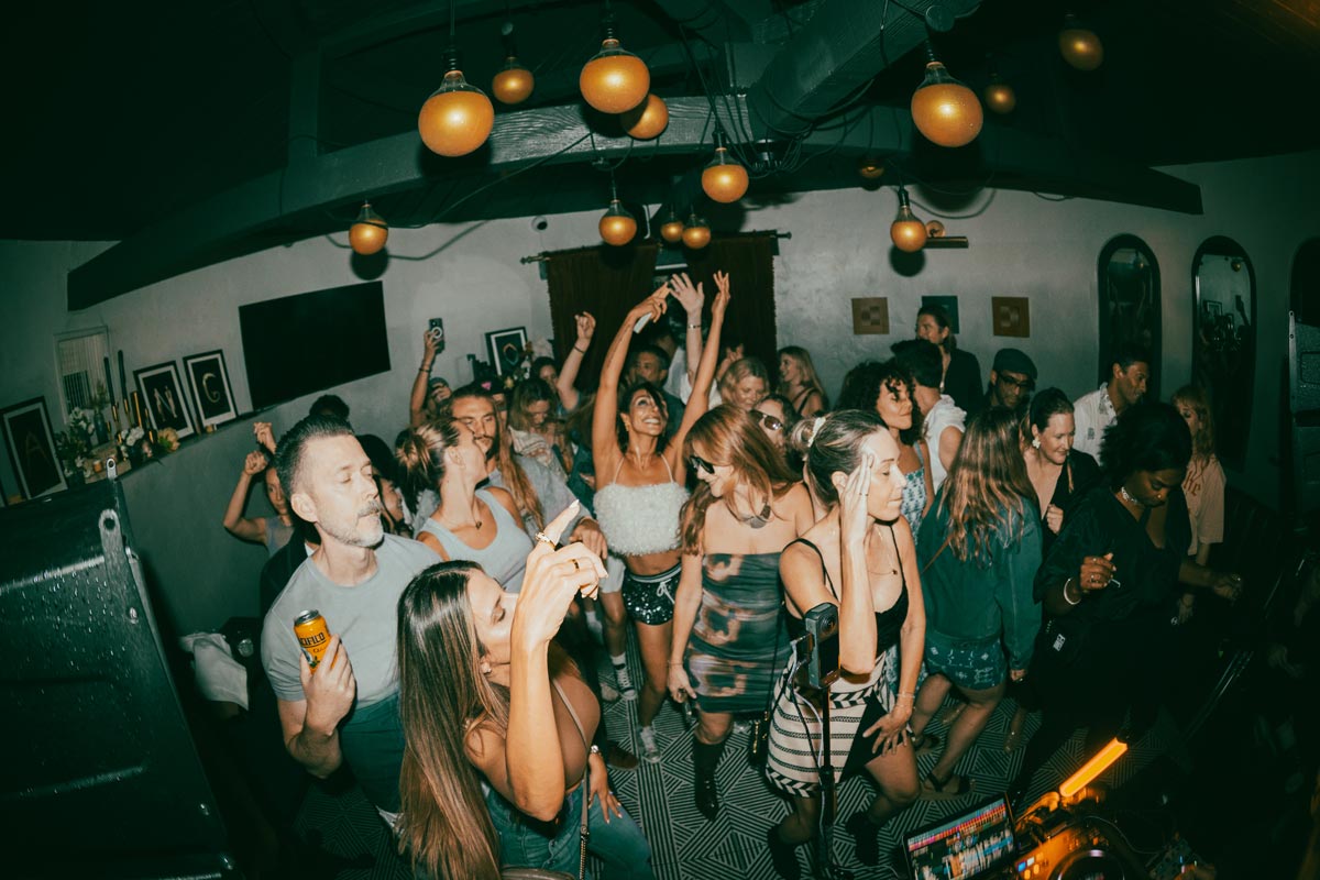 Guests raise their hands on a crowded dance floor beneath hanging globe lights.